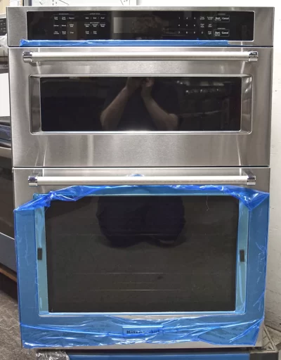 A front view of a brand new KitchenAid KOCE500ESS 30-inch Stainless Steel Built-In Microwave Combination Oven glass door with a blue protection film.