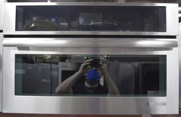 A front shot of a brand new Jenn-Air JMC2430DS 30-inch Euro-Style Stainless Steel Built-In Microwave Oven with a photographer's reflection on its glass door.